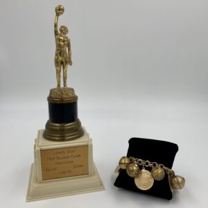 A gold trophy commemorating the history of women's basketball next to a gold bracelet.