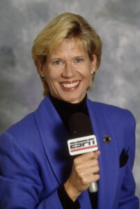 A woman in a blue jacket holding a microphone discussing the history of women's basketball.