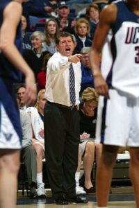 A coach pointing to a player on the court, demonstrating their expertise in women's basketball.