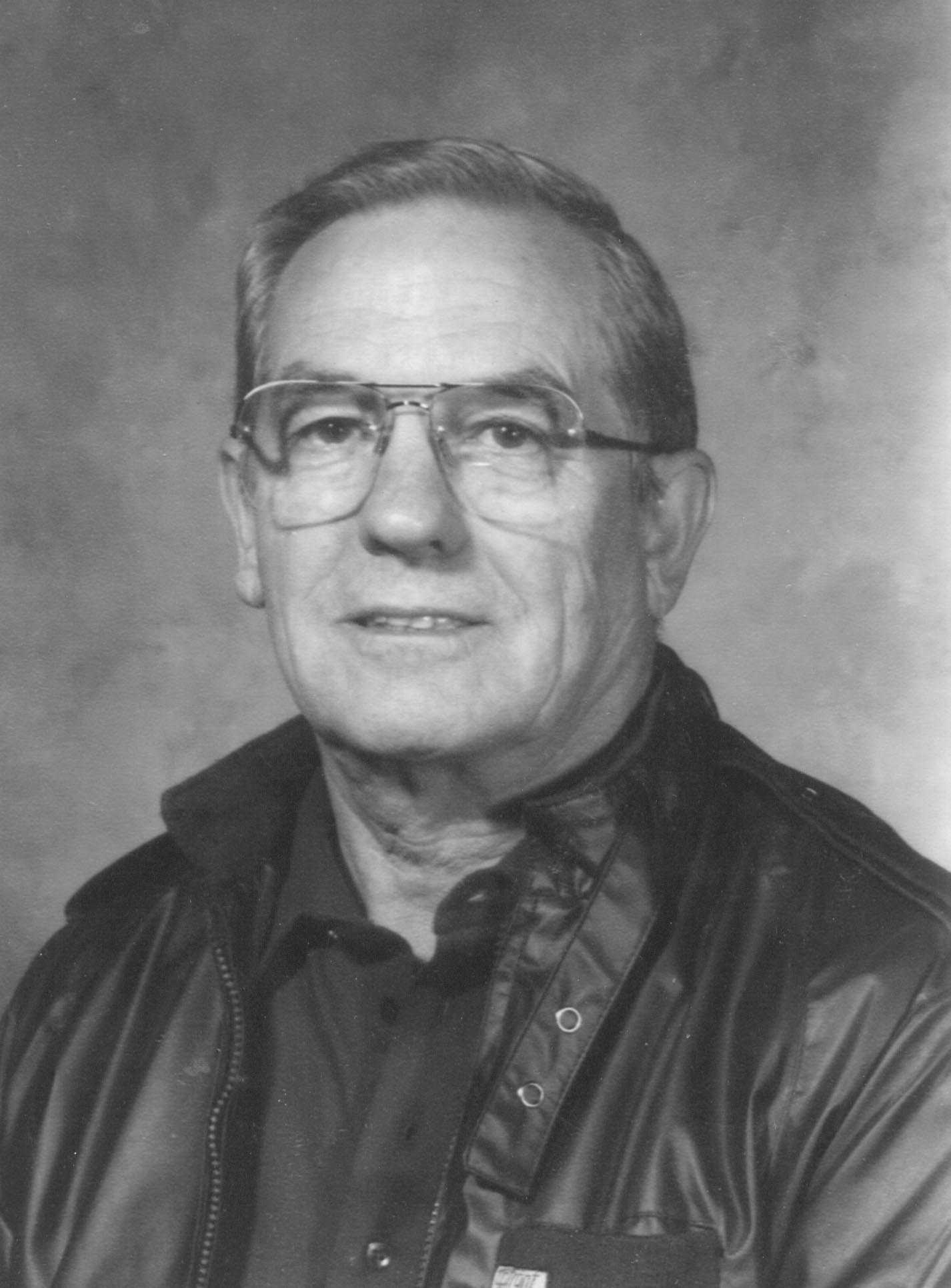 A black and white photo of an older man wearing glasses, reflecting the history of women's basketball.