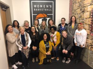 A group of women posing in front of a women's basketball sign.