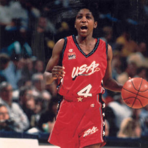 A woman in a red uniform, a pioneer in the history of women's basketball, holding a basketball.