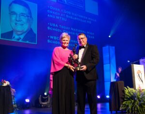 A man and woman proudly standing on stage, holding the prestigious Berenson Trophy.