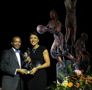 A couple posing next to a statue of a basketball player holding the Berenson Trophy.