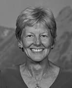 A black and white photo of a woman smiling in front of mountains.