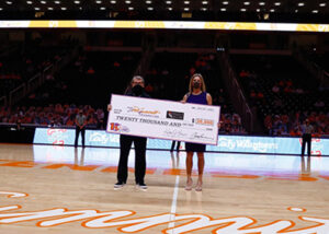 Two people standing on a basketball court holding a check.