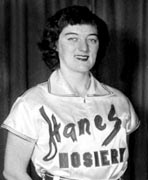 A black and white photo of a woman in a baseball uniform.