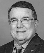 A black and white photo of a man wearing glasses and a suit.