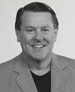 A black and white photo of a man smiling, reminiscent of women's basketball hall of fame members.