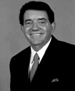 A black and white photo of a smiling man in a suit.