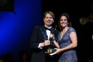 A man and woman standing next to each other holding the Berenson Trophy.